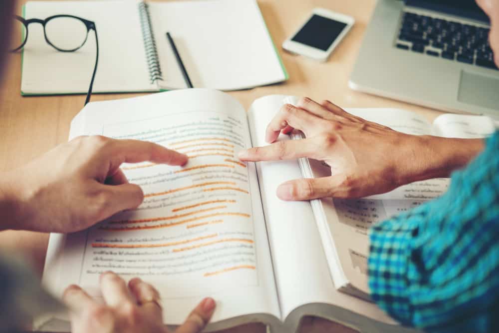 two people's hands pointing to page in textbook