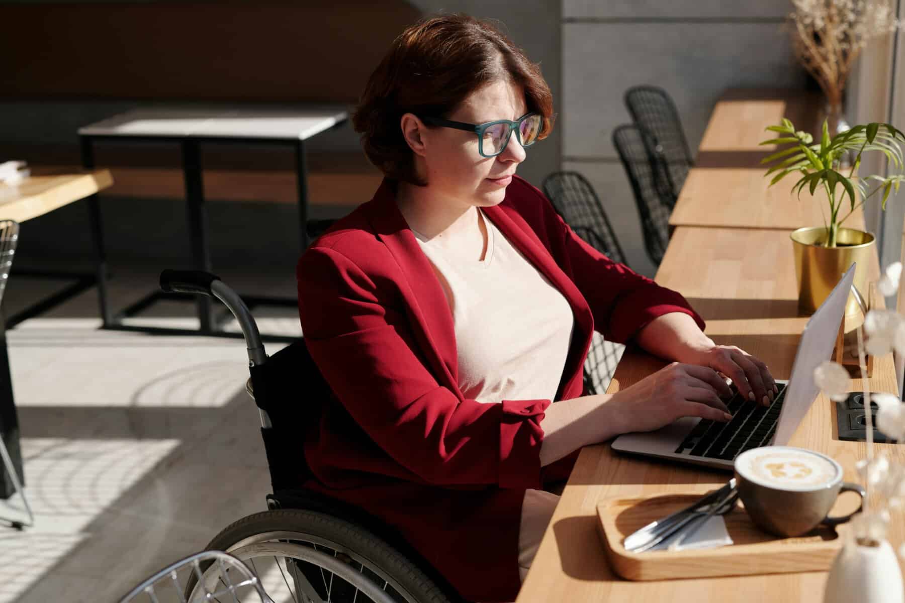 a woman in a wheelchair working at her computer drinking coffee
